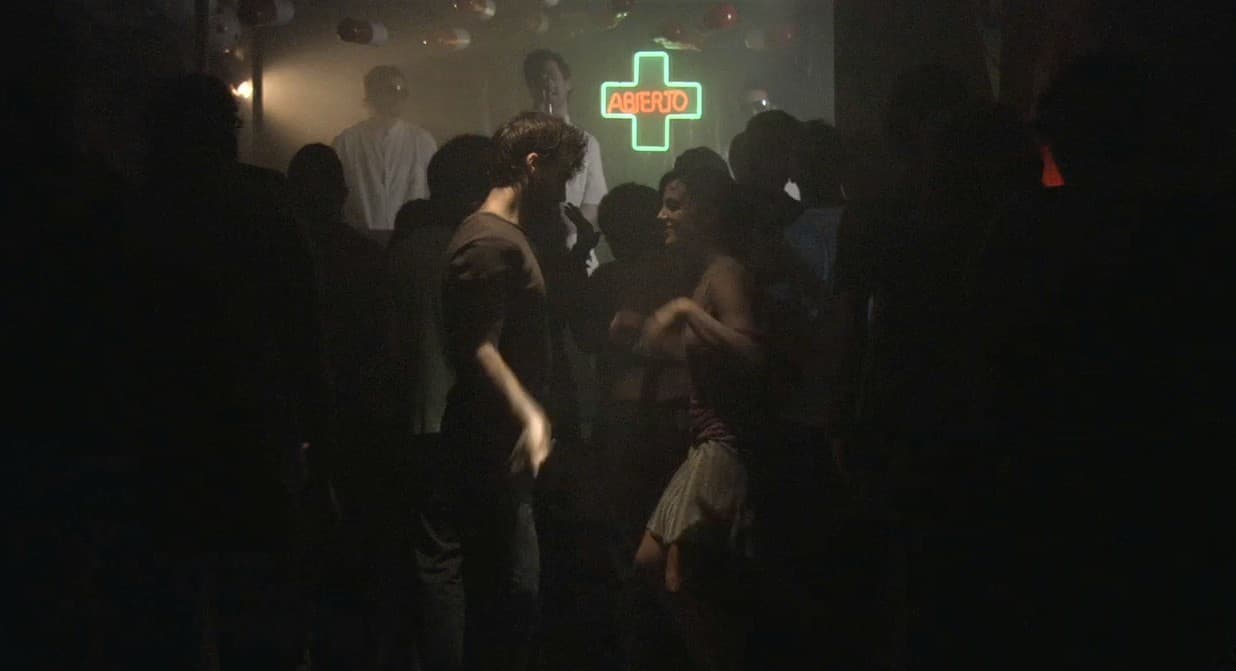 Grupo de personas en una escena nocturna oscura bajo una cruz luminosa verde.