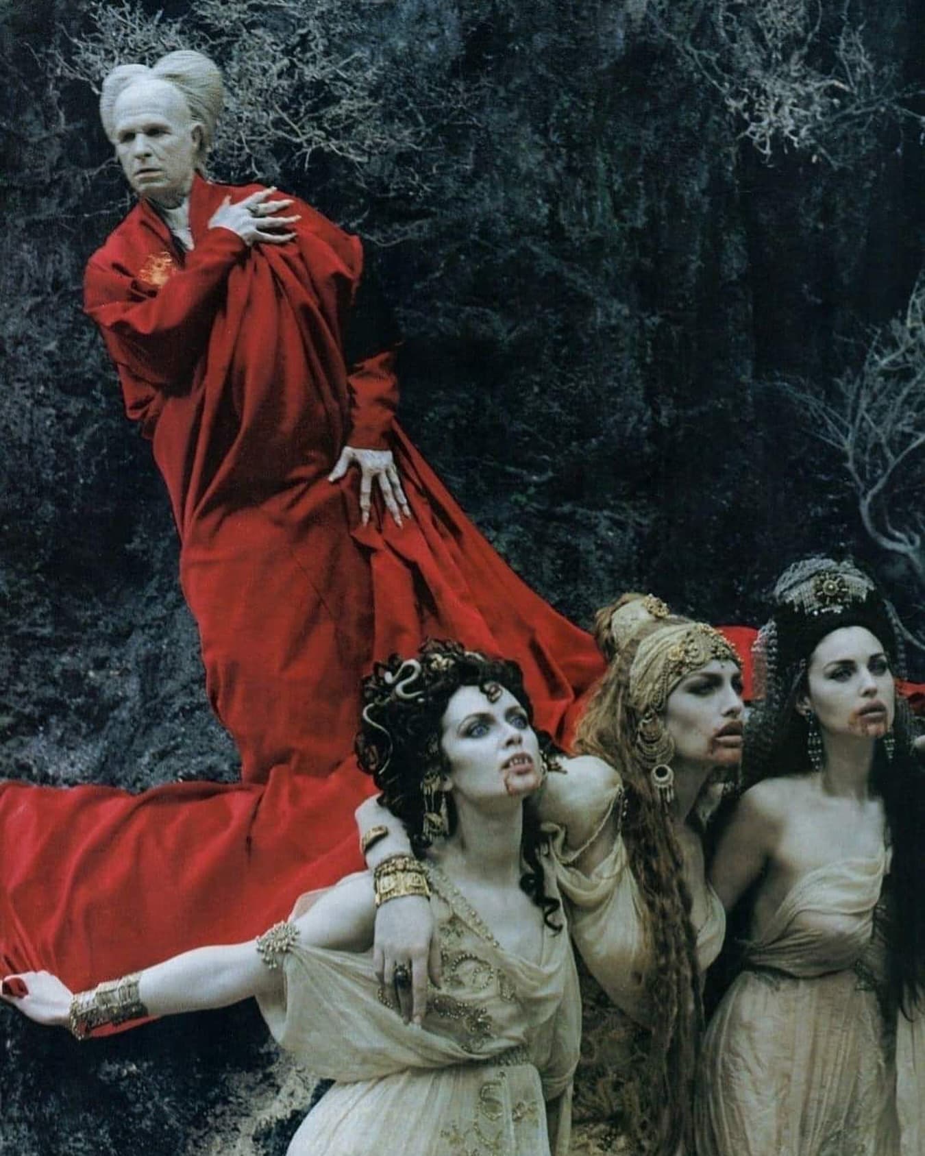 Group in theatrical costumes beside a figure in a red dress in a dark forest