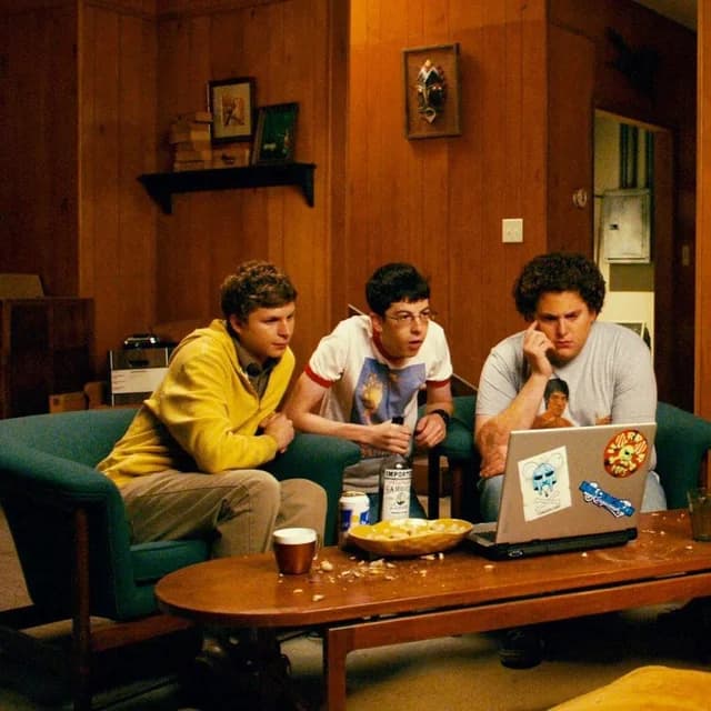 Three young men seated on a couch around a laptop in a wood-paneled room